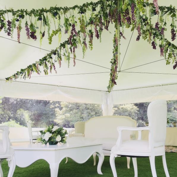 White wedding furniture under a canvas tent with beautifully arranged floral display on the ceiling