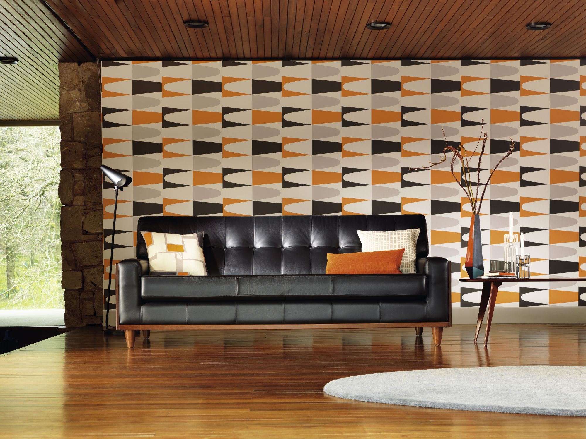 image of the G plan sofa which has a retro look to it due to the black leather sofa with orange cushions and geometric background